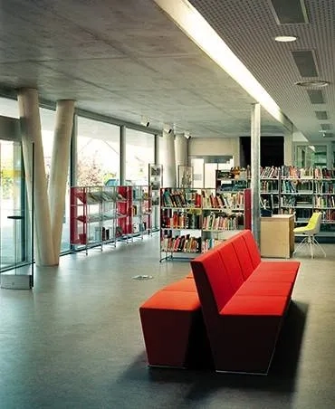 Hall d’entrée où s’avance la salle de lecture. le plafond béton, correspond à la partie du bâtiment de deux niveaux. une faille vitrée marque la transition avec la partie de plain-pied.