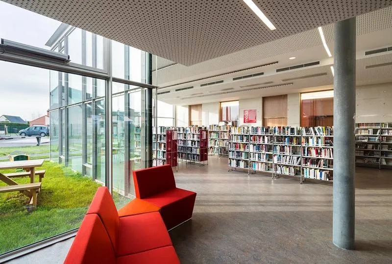 Salle de lecture et d’écoute de la médiathèque entièrement vitrée sur le jardin. les poteaux en béton implantés en retrait de la façade, signalent la structure.