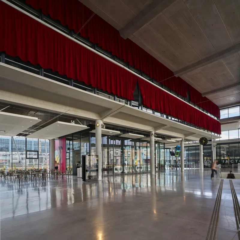 dans la continuité du hall, l’espace d’attente et d’accueil se glisse sous le premier niveau partiel de parking perceptible derrière les rideaux rouges.