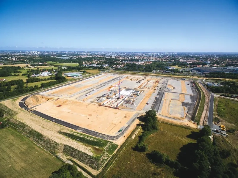 Deux vues aériennes du chantier, l’une en avril 2017 (où le traitement de plate-forme s’achève), l’autre deux mois plus tard, en juin 2017 (où la construction des premiers bâtiments commence).