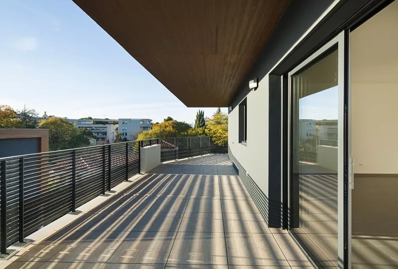 Vaste terrasse partiellement protégée par le porte-à-faux de l’attique qui fait brise-soleil. la matrice du béton et sa lasure brune s’accordent aux pins parasols.