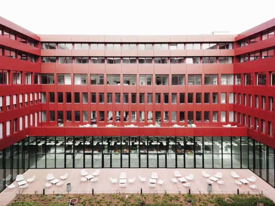 Le patio intérieur, point névralgique, à la fois poumon et cœur du campus, habillé de panneaux de façade en béton coloré d’un rouge intense.