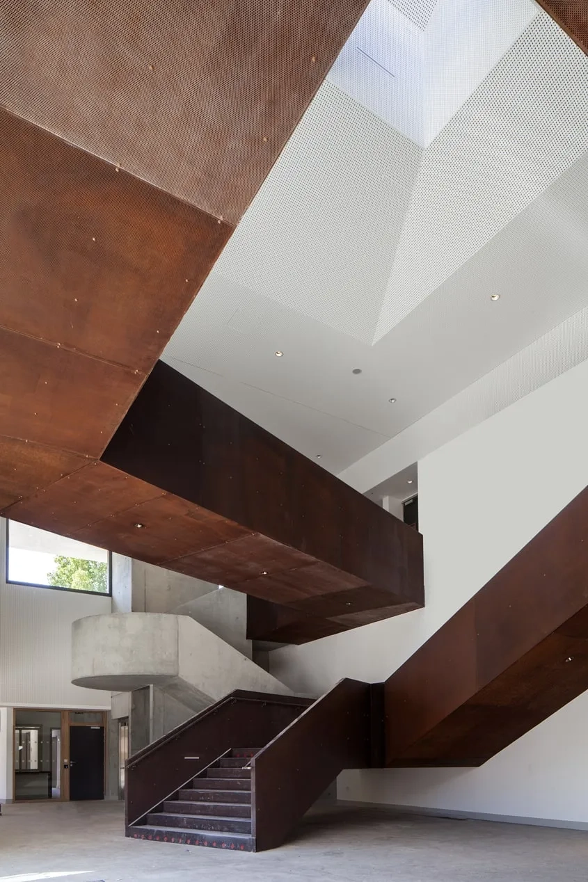 Le hall d’accueil double hauteur animé par ses deux escaliers, l’un en béton, l’autre en acier Corten, met en scène le parcours jusqu’à la salle de 600 places.